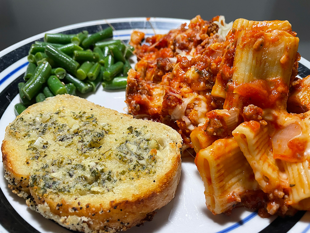 picture of a plate of food including homemade garlic bread, baked ziti and green beans
